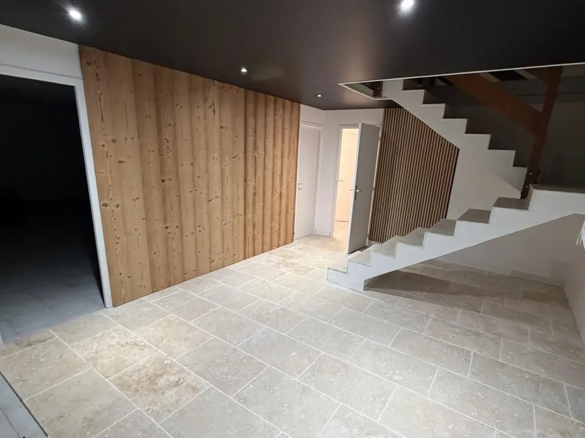 Entrée rénovée : sol travertin, bardage bois et plafond tendu noir