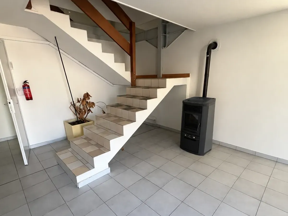 Entrée avant travaux : carrelage gris, escalier blanc et poêle à bois